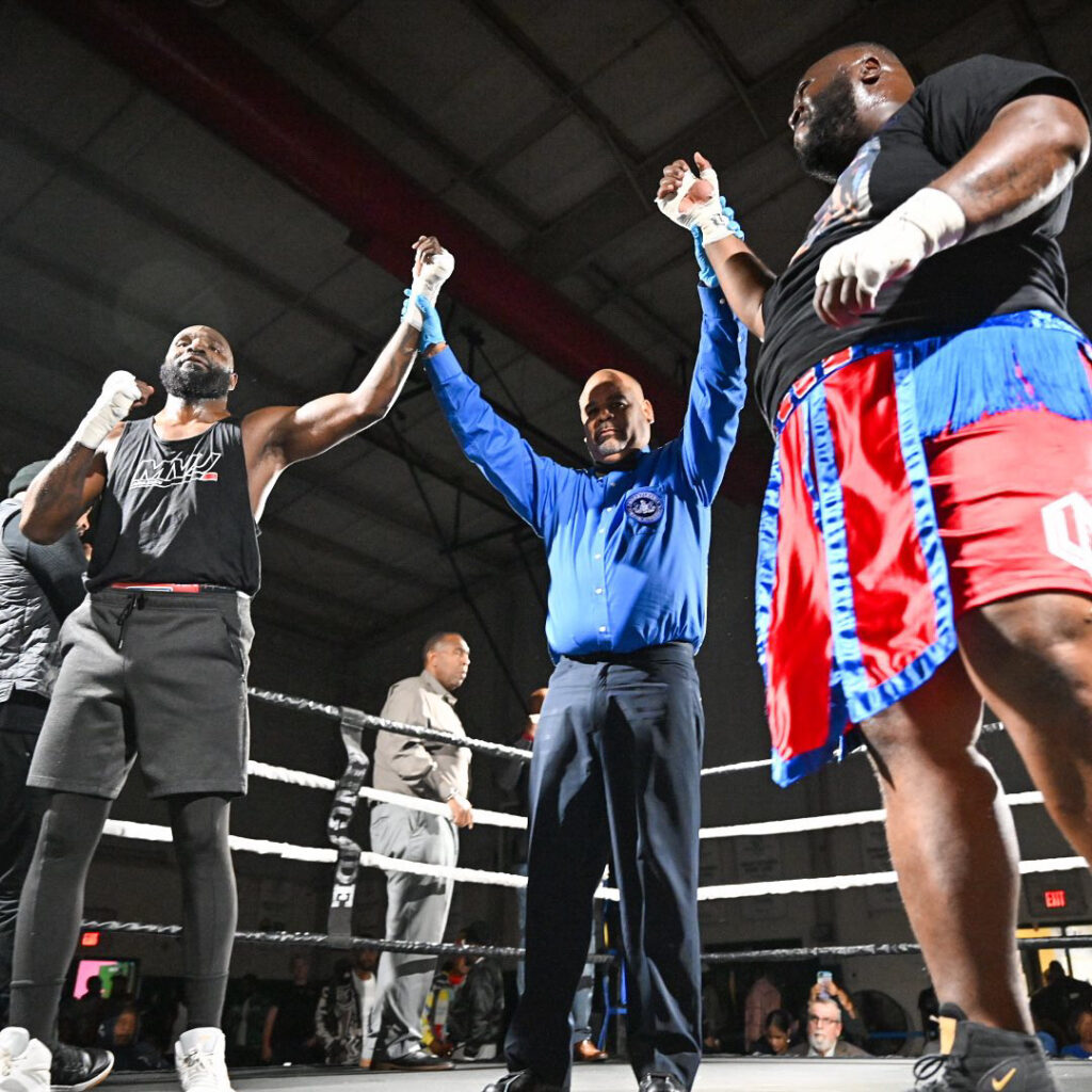 Referee holds the hands of both boxers while awaiting the judge's decision.